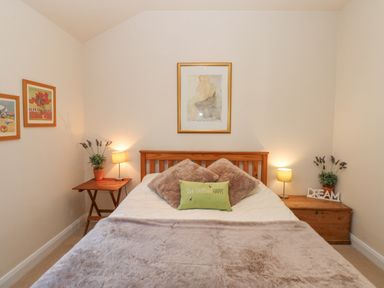 A bedroom with a bed a wooden headboard bedside tables table lamps wall art and decorative plants at Wellington Lodge Cottage in Middleton Tyas