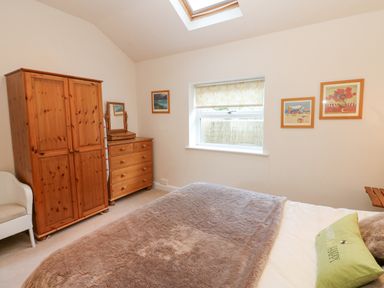 A bedroom with a wooden wardrobe and chest of drawers a bed with a fur blanket and a green pillow and framed pictures on the walls at Wellington Lodge Cottage in Middleton Tyas