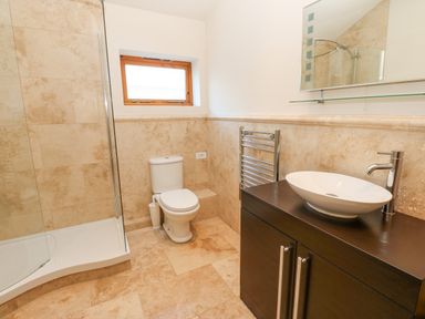 A bathroom with a toilet shower and sink on a dark wooden cabinet at Wellington Lodge Cottage in Middleton Tyas