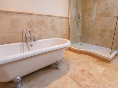 A bathroom with a freestanding bathtub and a walk-in shower with glass walls at Wellington Lodge Cottage in Middleton Tyas