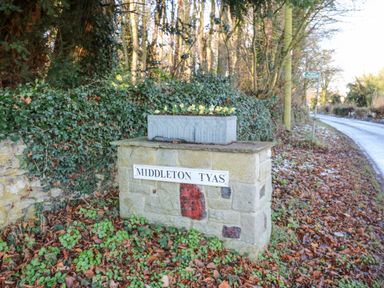A stone sign with the text Middleton Tyas next to a road and foliage at Wellington Lodge Cottage in Middleton Tyas