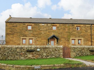 A stone house with multiple windows behind a stone wall with a wooden gate and green lawn at Winding Wheel Cottage in Cambois near Ashington