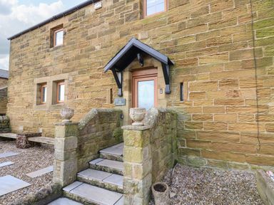 An exterior view of a stone house with steps leading to a wooden door at Winding Wheel Cottage in Cambois near Ashington