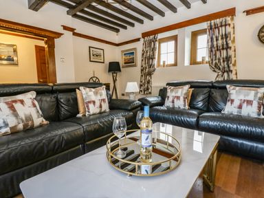 A living room with two black leather sofas cushions on sofas a coffee table with a bottle of wine and two wine glasses at Winding Wheel Cottage in Cambois near Ashington