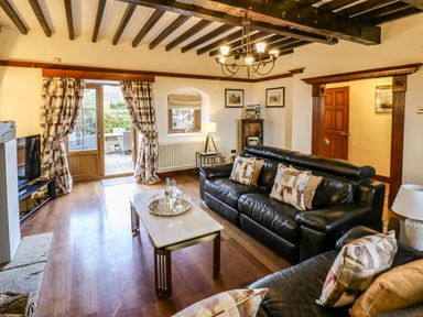 A living room with black leather sofas wooden beams and a coffee table at Winding Wheel Cottage in Cambois near Ashington
