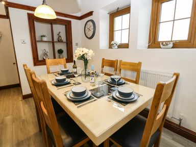 A dining room with a table set for six people with wooden chairs at Winding Wheel Cottage in Cambois near Ashington