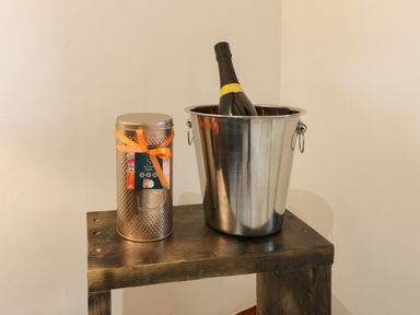 A metal ice bucket with a bottle inside and a decorated tin container with an orange ribbon on a wooden table at Winding Wheel Cottage in Cambois near Ashington