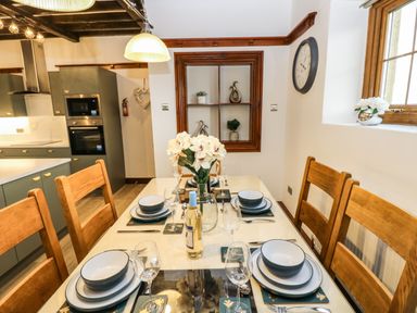 A dining table set for six with dishes glasses and a bottle of wine in a kitchen area at Winding Wheel Cottage in Cambois near Ashington