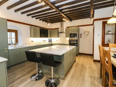 A kitchen with green cabinets a central island with stools and wooden ceiling beams at Winding Wheel Cottage in Cambois near Ashington