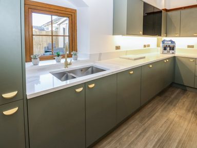 A kitchen with green cabinets a stainless steel sink and a wooden window at Winding Wheel Cottage in Cambois near Ashington