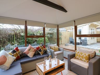 A sunroom with wicker sofas and chairs with cushions a small wooden table with wine glasses and a bottle at Winding Wheel Cottage Cambois near Ashington