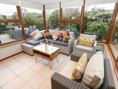 A sunroom with a corner sofa a chair a coffee table with wine and glasses surrounded by windows at Winding Wheel Cottage in Cambois near Ashington
