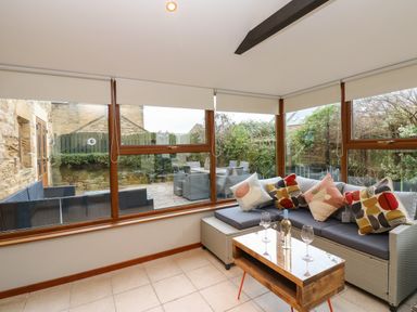 A sunroom with a sofa with cushions and a wooden coffee table with wine glasses and a bottle at Winding Wheel Cottage in Cambois near Ashington