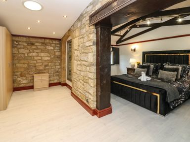 A bedroom with a black bed, wooden nightstand, stone wall, and wooden beam at Winding Wheel Cottage in Cambois near Ashington