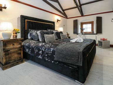 A bedroom with a large black and floral bed next to wooden nightstands with lamps and a telescope near a window at Winding Wheel Cottage in Cambois near Ashington