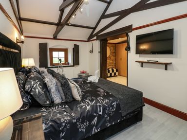 A bedroom with a bed pillows a wall mounted TV and a window with shutters at Winding Wheel Cottage in Cambois near Ashington
