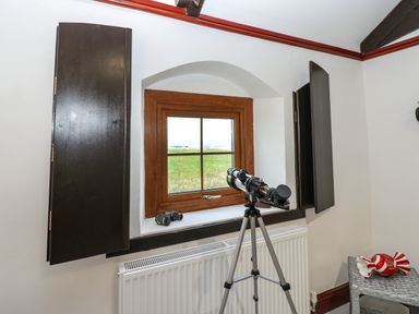A window with wooden shutters and a telescope on a tripod looking outside at Winding Wheel Cottage in Cambois near Ashington