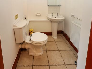 A bathroom with a toilet, pedestal sink, radiator, and tiled floor at Winding Wheel Cottage in Cambois near Ashington