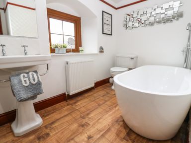 A bathroom with a freestanding bathtub a toilet a pedestal sink a window with flowers and a decorative mirror at Winding Wheel Cottage in Cambois near Ashington