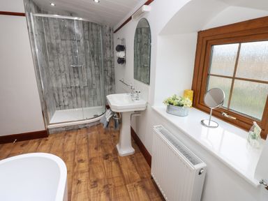 A bathroom with a shower, sink, window with a mirror and radiator at Winding Wheel Cottage in Cambois near Ashington