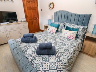 A bedroom with a patterned bedspread on a bed with blue headboard and folded towels on top at Winding Wheel Cottage in Cambois near Ashington