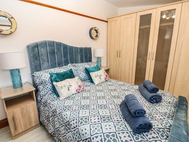A bedroom with a double bed and patterned bedding two bedside tables with lamps and a large wooden wardrobe at Winding Wheel Cottage in Cambois near Ashington