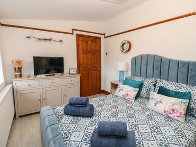 A bedroom with a patterned bedspread TV on cabinet and wooden door at Winding Wheel Cottage in Cambois near Ashington