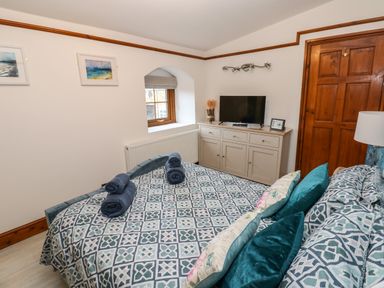 A bedroom with a patterned bedspread and rolled towels on the bed a dresser with a television a wooden door and two framed pictures on the wall at Winding Wheel Cottage in Cambois near Ashington