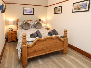 A bedroom with a wooden bed and nightstands with lamps and framed pictures on the walls at Winding Wheel Cottage in Cambois near Ashington