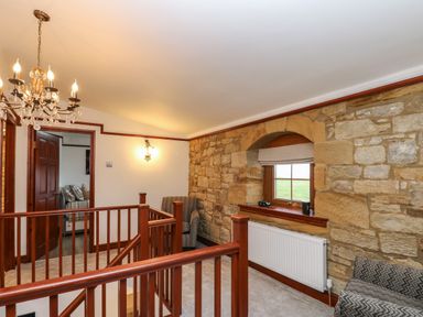 A hallway with wooden staircase railing stone wall and window with armchairs at Winding Wheel Cottage in Cambois near Ashington