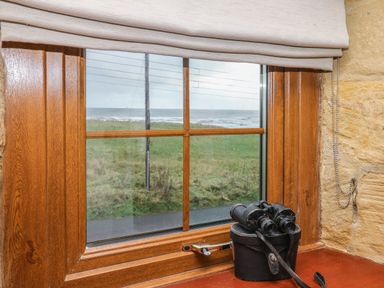 A wooden window with binoculars on a ledge looking out to grass and sea at Winding Wheel Cottage in Cambois near Ashington