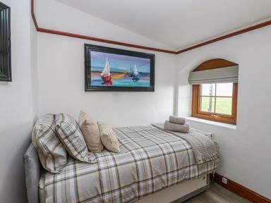 A bedroom with a single bed with plaid bedding a window with a blind and a framed painting of sailboats on the wall at Winding Wheel Cottage in Cambois near Ashington