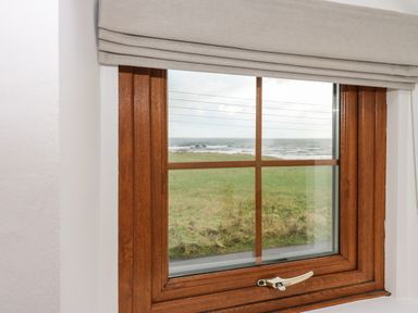 A wooden framed window with a beige blind showing a grassy field and sea beyond at Winding Wheel Cottage in Cambois near Ashington