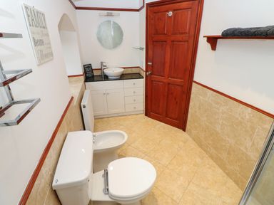 A bathroom with a toilet bidet sink and wooden door at Winding Wheel Cottage in Cambois near Ashington