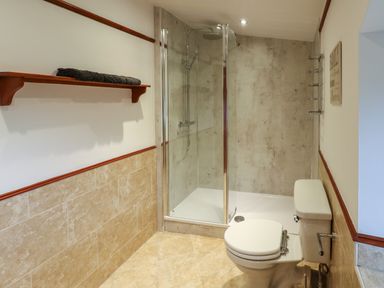 A bathroom with a toilet a glass shower enclosure and a wooden shelf with a towel at Winding Wheel Cottage in Cambois near Ashington
