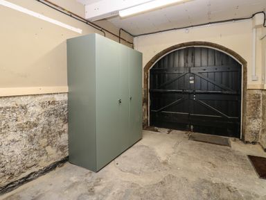 A garage with a large green storage cabinet and black double wooden doors at Winding Wheel Cottage in Cambois near Ashington