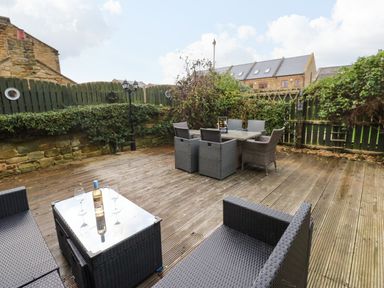 An outdoor patio with wicker chairs a table with a bottle and glasses surrounded by fences and plants at Winding Wheel Cottage in Cambois near Ashington