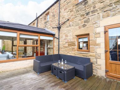 An outdoor patio with wicker seating and a glass table with wine glasses at Winding Wheel Cottage in Cambois near Ashington