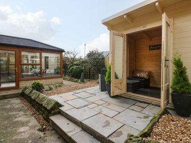 A garden area with stone steps leading to a wooden garden room and a glass conservatory at Winding Wheel Cottage in Cambois near Ashington
