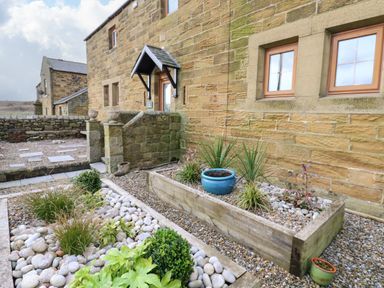 An outdoor stone patio area with raised wooden planters containing plants and pebbles at Winding Wheel Cottage in Cambois near Ashington