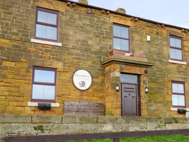 Exterior of a stone building with six windows a wooden door and a sign reading Charltons Cambois Beach at Winding Wheel Cottage in Cambois near Ashington