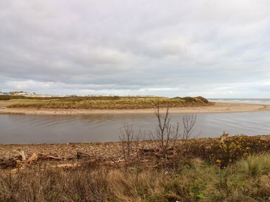 A river flowing into the sea with sandy dunes and grass along the shore at Winding Wheel Cottage in Cambois near Ashington