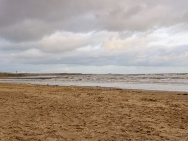 A sandy beach with waves and a cloudy sky at Winding Wheel Cottage in Cambois near Ashington