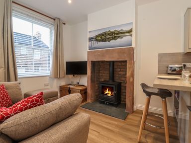 A living room with a fireplace a television and a kitchen bar stool at Jack's Cottage in Keswick