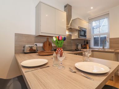 A kitchen with a wooden countertop set with two plates glasses utensils a vase with artificial flowers stainless steel toaster microwave and sink at Jacks Cottage in Keswick