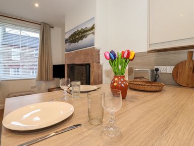 A kitchen dining area with plates glasses a vase with artificial flowers and a fireplace at Jacks Cottage in Keswick