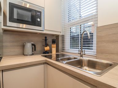A kitchen corner with a microwave a kettle a knife block a double sink and a window with blinds at Jack's Cottage in Keswick