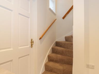 A carpeted staircase with wooden handrails and a white door next to it at Jacks Cottage in Keswick