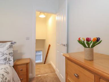 A bedroom with a wooden nightstand next to a bed and a wooden chest of drawers with a vase of flowers at Jacks Cottage in Keswick