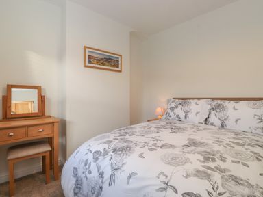 A bedroom with a double bed with floral bedding a wooden dressing table and a landscape picture on the wall at Jacks Cottage in Keswick